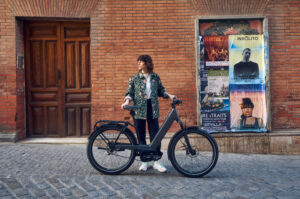 Riese & Müller Nevo5 Pinion elsykkel med lavt innsteg, sideprofil ved murvegg i bymiljø